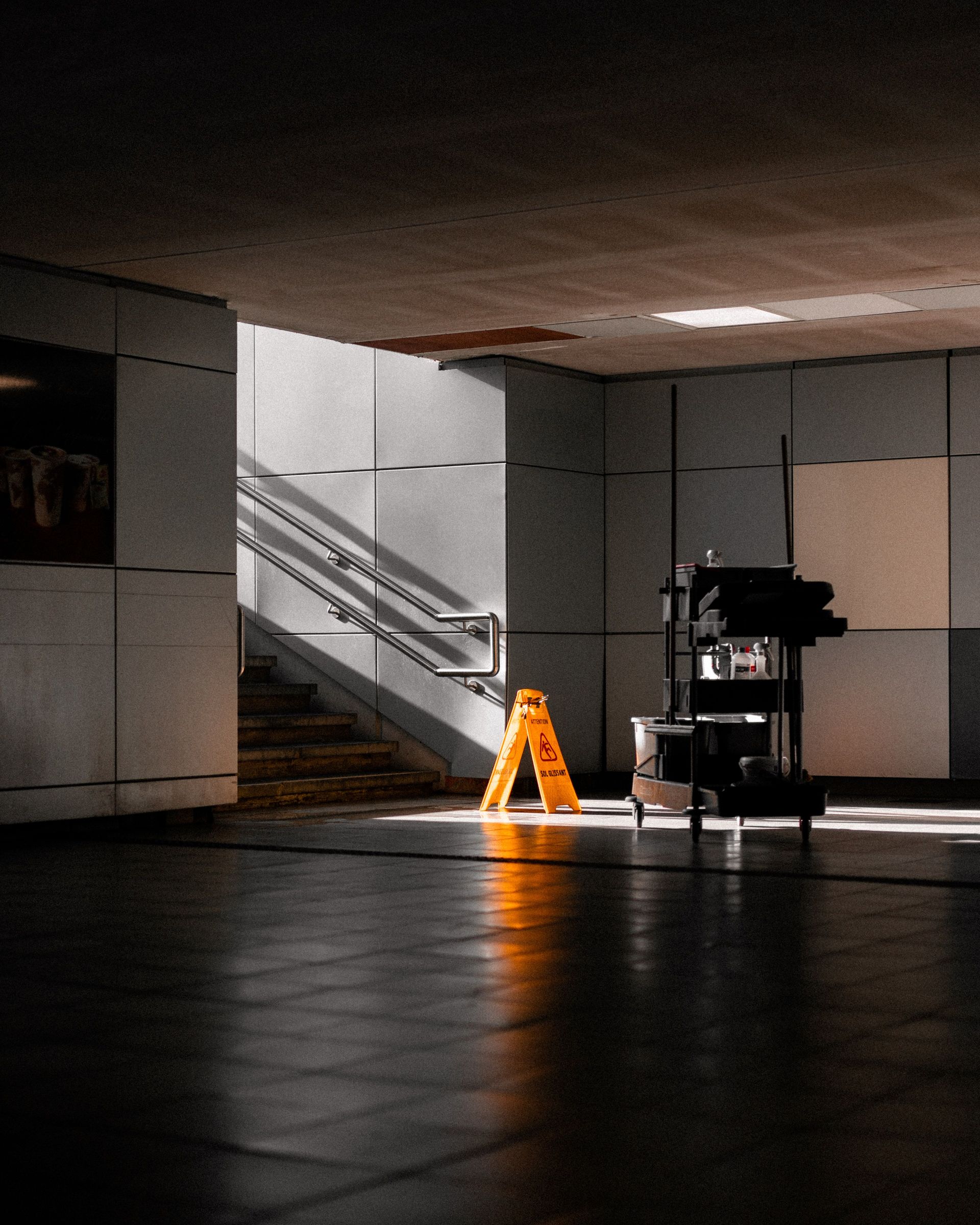 A well-lit underground corridor featuring stairs, cleaning supplies, and warning signs.